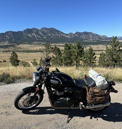 a black and gold triumph cafe motorcycle, pulled over on dirt overlooking a gorgeous rocky mountain vista